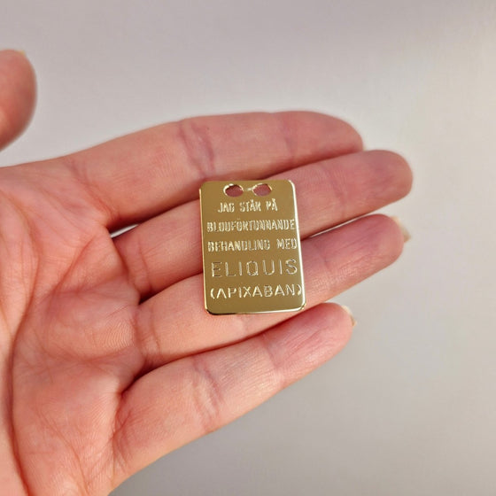 Eliquis bricka i förgyllt silver 27x19mm